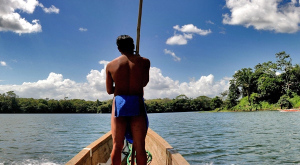 Sentralamerikanske guide som fører båten. Elv, blå himmel, skyer og grønn skog.