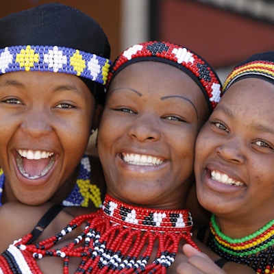 Tre unge Zulu-venninner, kledd i tradisjonelle Zulu-klær, poserer lykkelig for kameraet. Zulu-stammen finnes hovedsakelig i Kwazulu-Natal, Sør-Afrika.