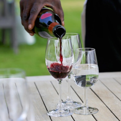 Servitør som heller rødvin i et glass for vinsmaking. Et glass vann står også på bordet.