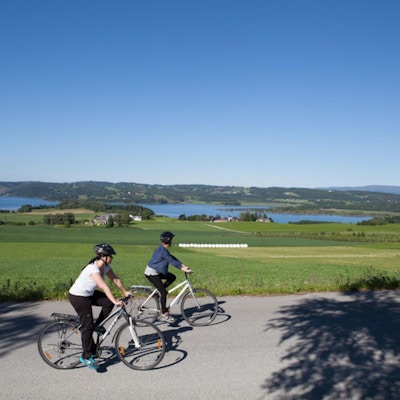 to syklister ute på tur med hjelm og fritidsklær. Utsikt over grønne sletter og vann