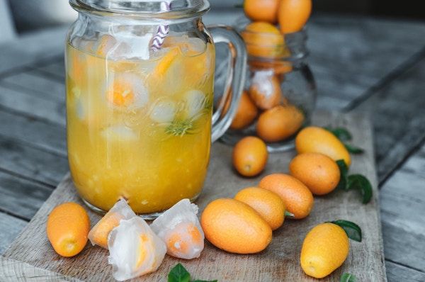 Glasskar med appelsinjuice med is og kumquat på trebord