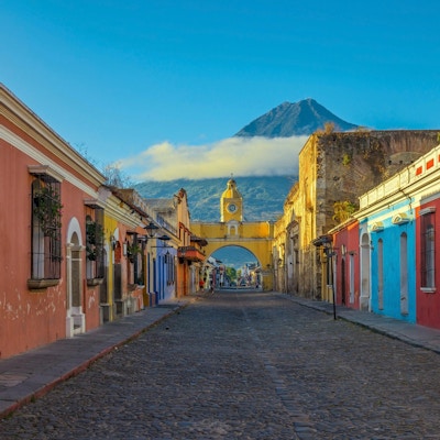 Den historiske byen Antigua ved soloppgang med utsikt over hovedgaten og Catalina-buen og vulkanen Agua i bakgrunnen, Guatemala.