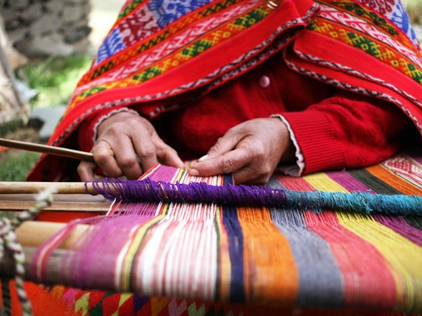 Et nærbilde av en kvinne som vever i Peru med lyse tradisjonelle klær.