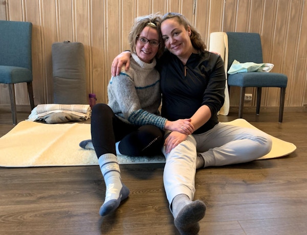 To kvinner med armene rundt hverandre på yogamatte.
