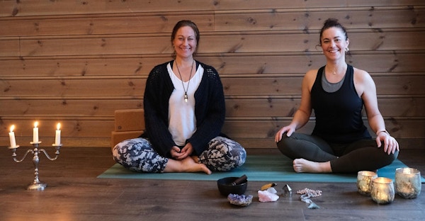 To damer sitter i lotusstilling på yogamatte.