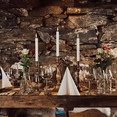 Bord rustikt pyntet til fest med lys, servietter, glass og blomster foran en dekorativ vegg av stein i vinbaren Nes Bar