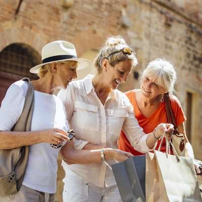 En kvinne står i en gammel del av byen i Italia og holder på med handleposer. Hun viser de to vennene sine hva hun har kjøpt. Alle tre smiler mens de står side om side