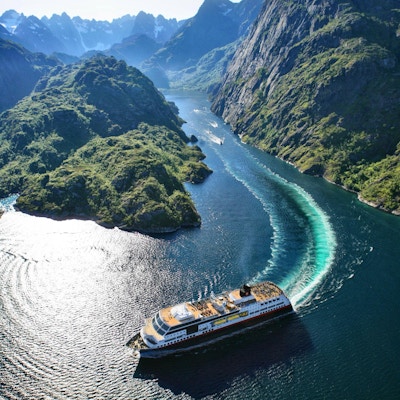 Skip kommer ut av trang fjord med spisse fjell.