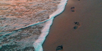 en person som går langs stranden og lager fotavtrykk i sanden
