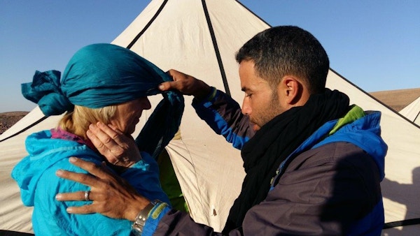 Kvinne får bistand med blått hodeklede forran telt i ørkenen