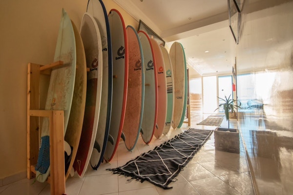 Stativ med surfebrett i ulike farger, solfylt gangparti