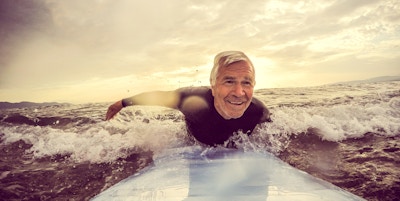 Veldig aktiv senior mann, surfer på en bølge med et surfebrett