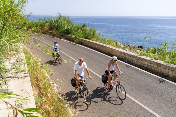 Tre personer sykler på asfaltert vei langs kysten av Puglia