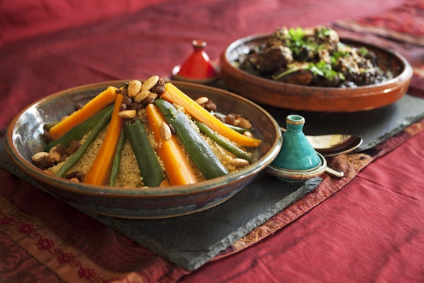 Vegetabilske couscous og kjøtt- og svisketagine pyntet med fersk koriander og sesamfrø. Autentisk pepper og saltgryter og duker.