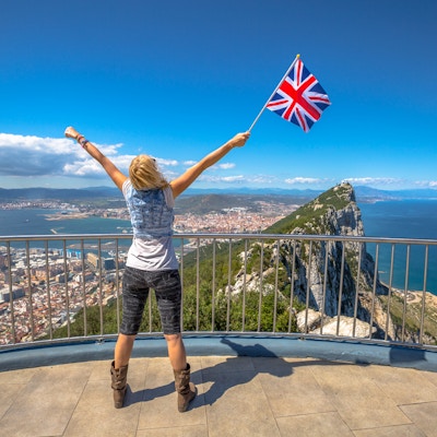 Kvinne med det britiske flagget i hånden på toppen av Gibraltar Rock. Gibraltar er et territorium i Sør-Vest-Europa som er en del av Storbritannia.