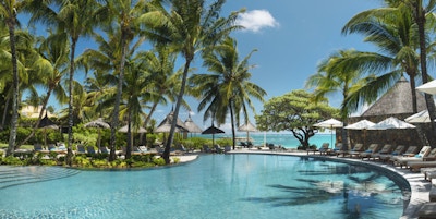 Resort med basseng, palmer, og hav.