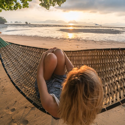 Ung kvinne på en tropisk hage i Thailand som ligger på en hengekøye som slapper av. Solnedgangstid på øya.