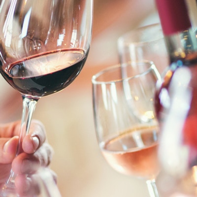 Nærbilde av ugjenkjennelige voksne som holder glass vin og utfører visuell undersøkelse. Evaluering av utseende, farge, klarhet, rester på glasset. Det er vinflasker og andre vinprøver i bakgrunnen.