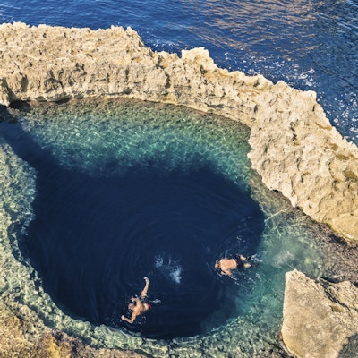Dypblått hull ved det verdensberømte Azure Window på Gozo-øya - middelhavsunderrund på det vakre Malta - Ukjennelige turistdykkeere som svømmer til vannvannhule