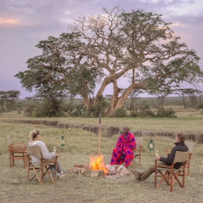 Par sitter rundt bålet på savannen  sammen med en masai.