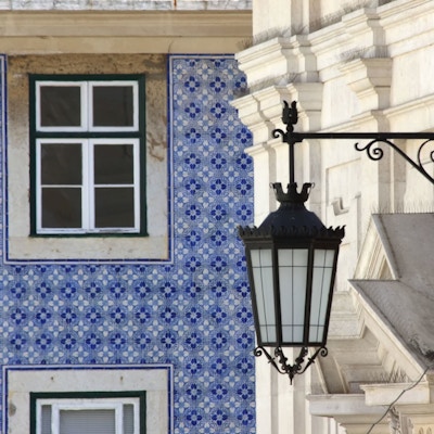 Husvegg dekket av blå og hvite fliser. En stor gatelykt med dekor henger utenfor