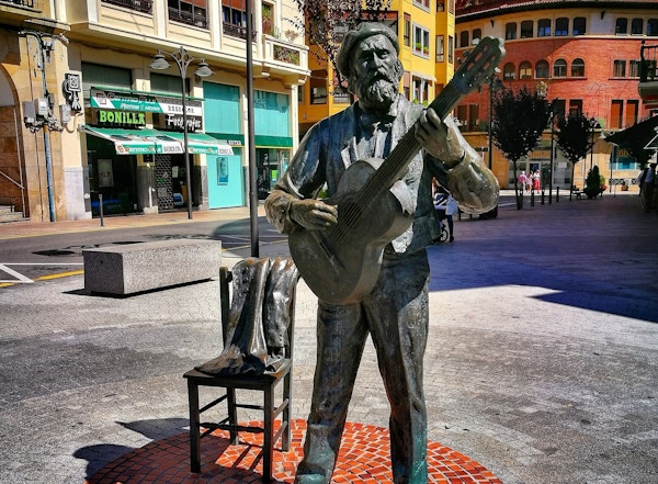 Statue  av mann som spiller gitar på torg i by.