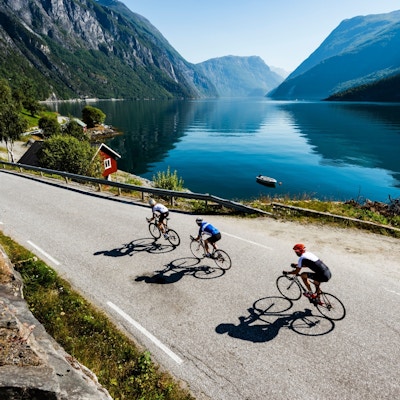 3 sykkelister som sykler på en vei langs havkananter ved den nydelige Geirangerfjorden
