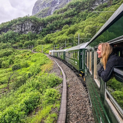 Kvinne ser ut av togvindu mens toget kjører gjennom grønt fjellandskap.