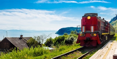 Landskap for reise med ankomsten av et rødt tog på en tre øde plattform Circum-Baikal jernbane i en landsby ved Baikal-sjøen i en lys solskinnsdag.