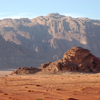 Kveldslandskap i Wadi Rum-ørkenen med kjøretøyspor i sanden.