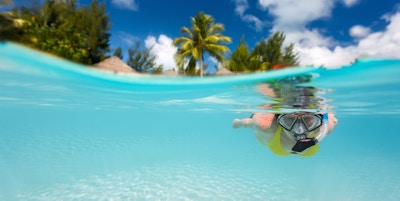 Kvinne svømmer under vann i klart tropisk vann foran eksotisk øy