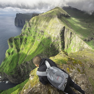 En mann som sitter på toppen av et fjell og ser på den vakre naturen.