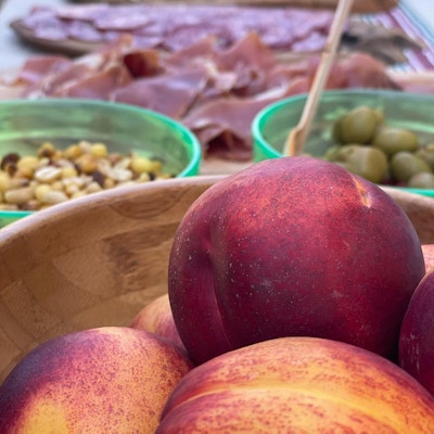 her ser man noe av maten som er på piknik bordet som blant annet nektariner, oliven, skinke og ost
