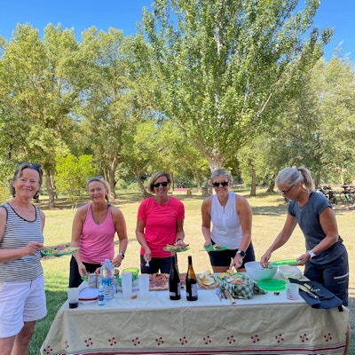5 damer forsyner seg med mat fra et dekket piknik bord ute i naturen