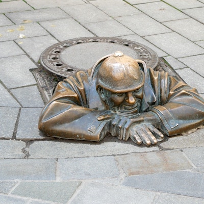 Statue av mann som kryper opp av kumlokk