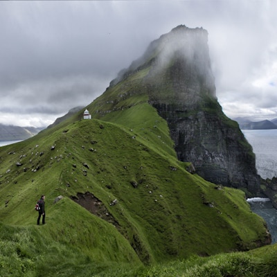 Mann ser utover utsikt mot havet, fyrtårn ofg fjell i bakgrunnen