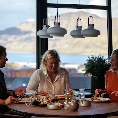 Tre kvinner spiser på restaurant med panoramavinduer med fjellandskap utenfor.