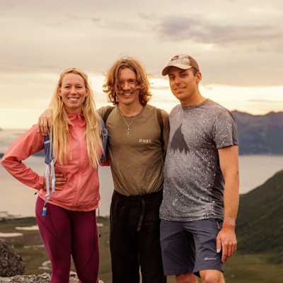 Tre unge mennesker på fjelltop med hav i bakgrunnen.