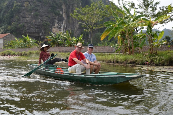 Vietnamesisk dame i robåt med to menn, hvor hun ror med beina.