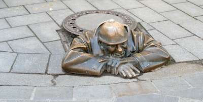 Statue av mann som kryper opp av kumlokk