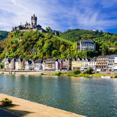 Liten middelalderby ved elvebredden med en gammel borg på toppen.