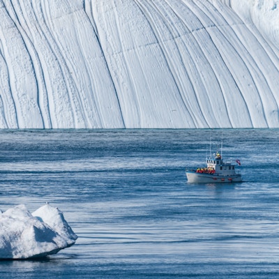 En liten båt med turister ligger i havet mellom isfjellene utenfor Ilulissat