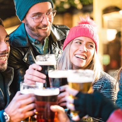 Venner drikker øl på bryggeribaren utendørs om vinteren - Vennskapskonsept med unge mennesker som har det gøy sammen og skåler på happy hour-kampanje - Fokus på jente med rosa hatt - Varmt neonfilter