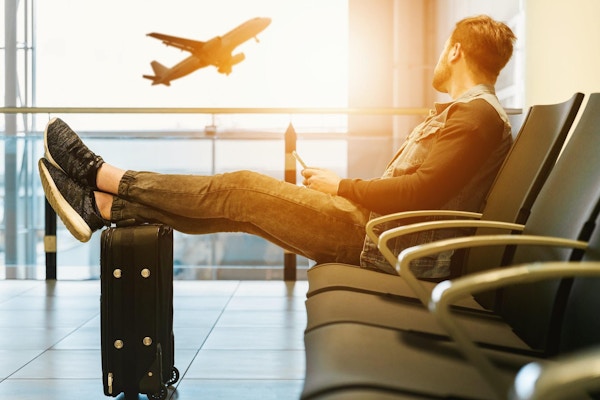Mann sitter med beina på en koffert og venter, på en flyplass