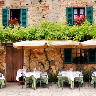 Kafébord og stoler utenfor en sjarmerende steinbygning i Toscana, Italia