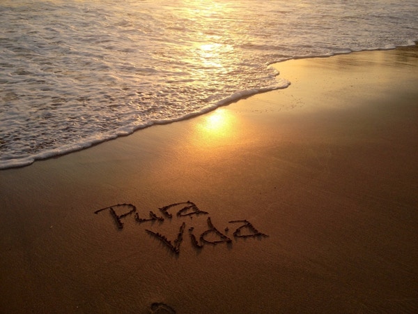 En strand ved solnedgang med uttrykket "pura vida" skrevet i sanden