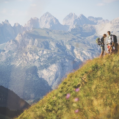 Fjellvandrere står i en grønn fjellside med et fantastisk fjellandskap i bakgrunnen.