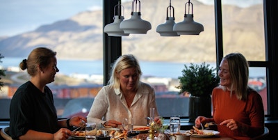 Tre kvinner spiser på restaurant med panoramavinduer med fjellandskap utenfor.