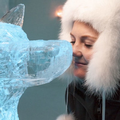 Jente med pelslue setter nesen sin mot nesen på en isskulptur av en hund