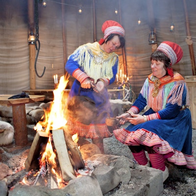 To samekvinner i kofte koker kaffe på bålet i lavvoen